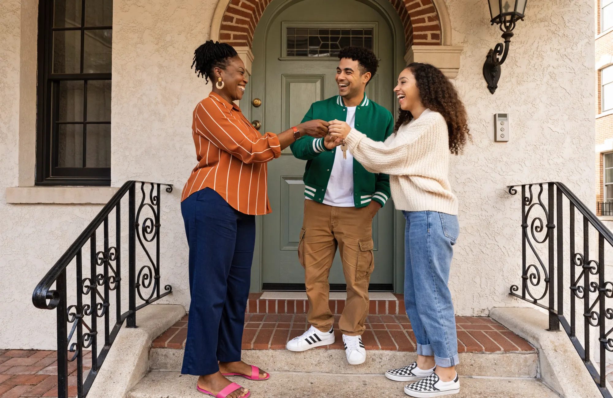Une agente remet en souriant les clés de leur nouvelle maison à un jeune couple, sur le perron