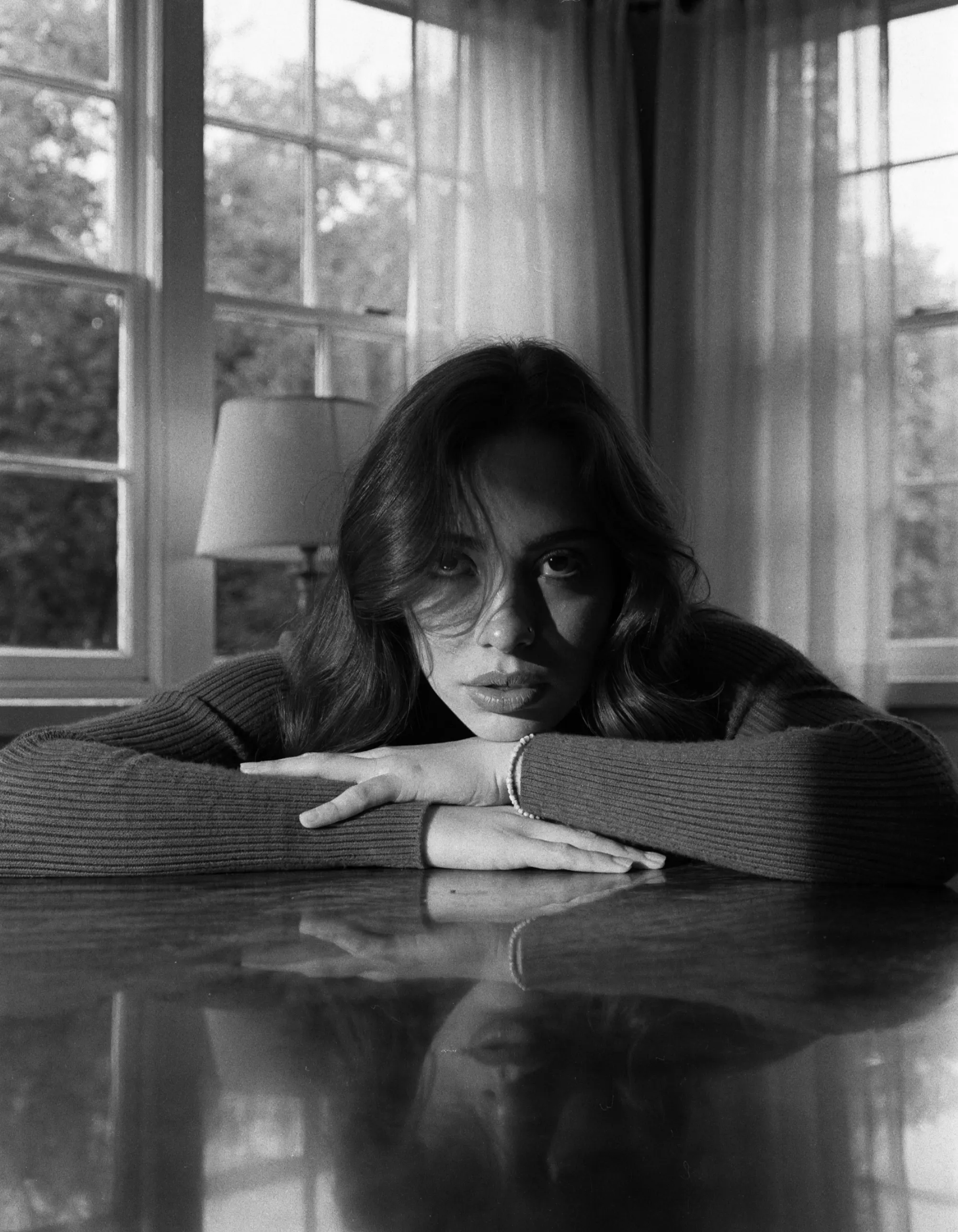 Portrait en noir et blanc d’une jeune femme accoudée à une table, près d’une fenêtre