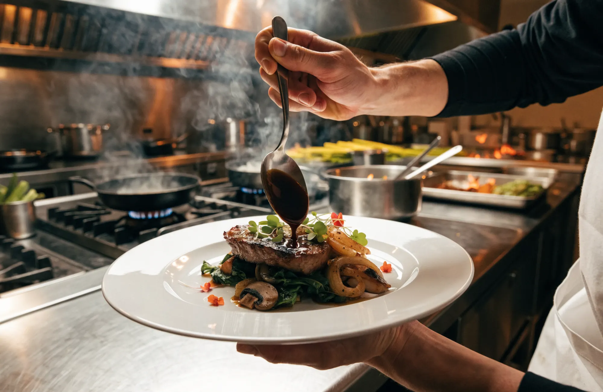 La cheffe dresse une assiette dans la cuisine ouverte, flammes et casseroles en cuivre en arrière-plan